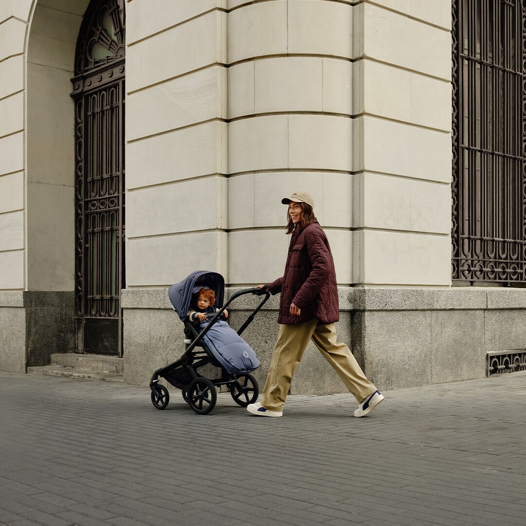 Frau schiebt Kind im Kinderwagen an Gebäude vorbei