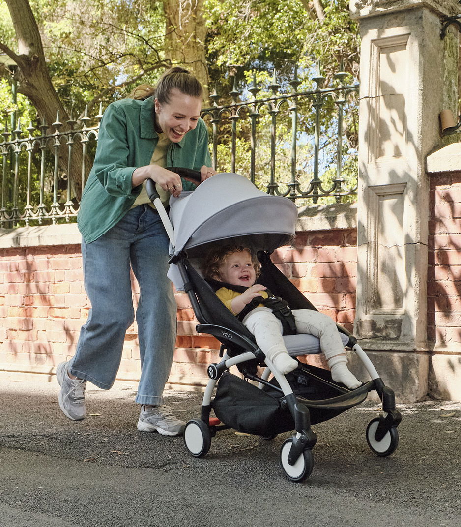 Lachendes Kind in einem Kinderwagen, geschoben von einer fröhlichen Mutter im Freien.